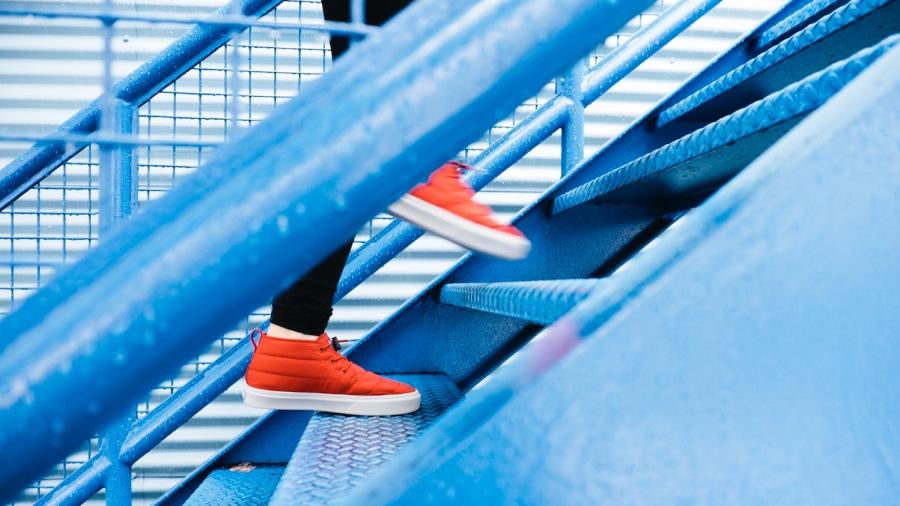 Dame met rode sneakers klimt een blauwe trap op