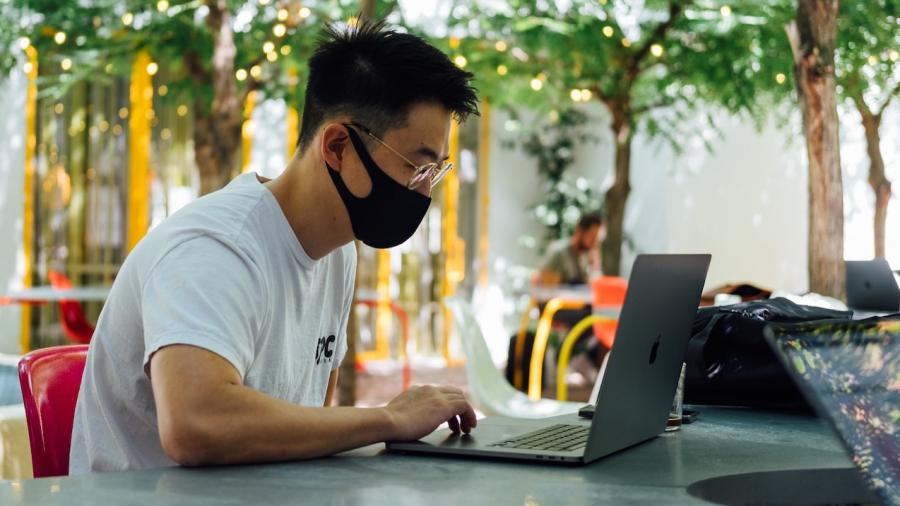Man met mondmasker surft op een plein op zijn laptop