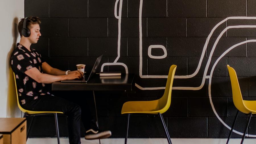 Een student met hoofdtelefoon werkt vanuit een hippe coworking met gele stoelen
