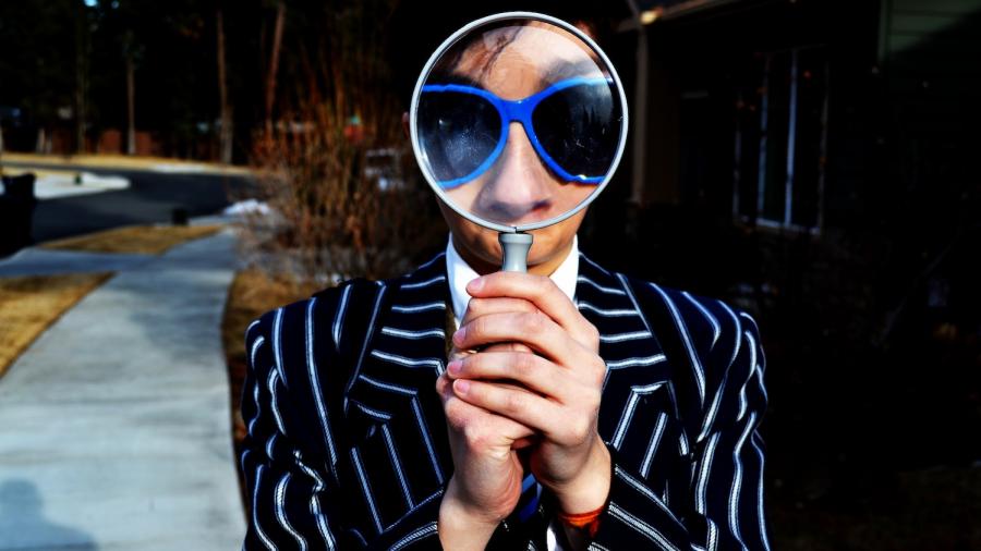 Man met een grote blauwe bril kijkt door een vergrootglas